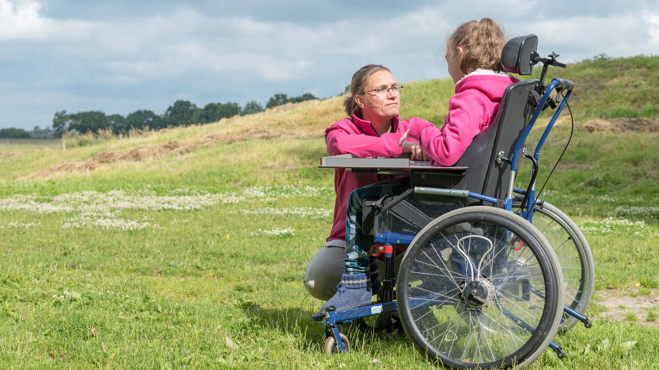 En gehandicapte kind in een rolstoel samen buiten met een verpleegkundig zorgverlener