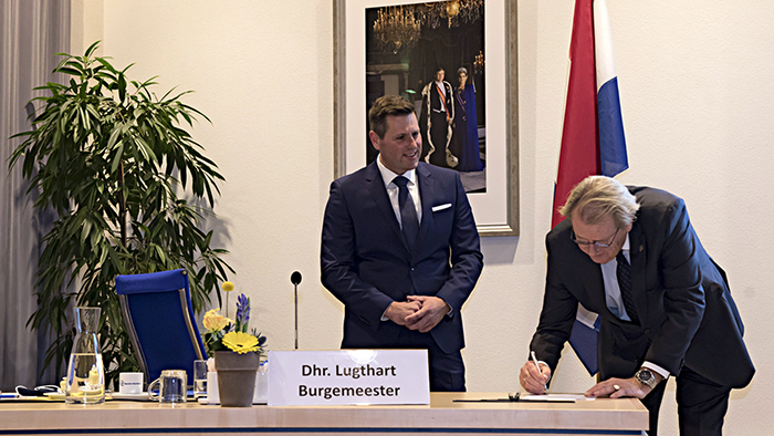 Commissaris van de koning Jaap Smit tekent het beëdigingsdocument terwijl burgemeester Lugthart toekijkt.