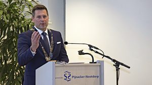 burgemeester Björn Lugthart speecht achter een katheder met daarop het logo van de gemeente Pijnacker-Nootdorp